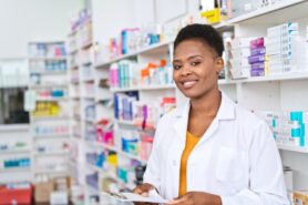 Smiling pharmacy tech standing in front of shelves with medication 