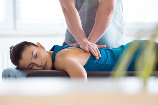 Massage therapist giving back massage to young patient lying on massage table