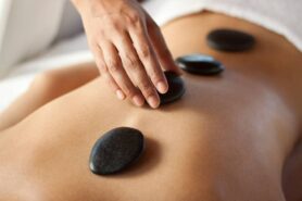 Hands massaging lower back with warm stones